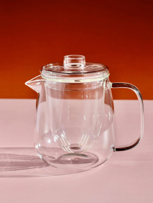 Glass tea pot with infuser on a table with pink and read background