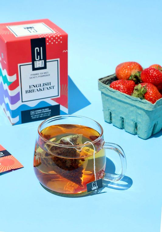Teacup with pyramid teabag inside, in the background a box of English Breakfast Tea and strawberries