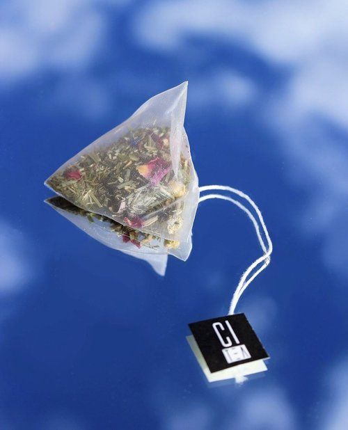 Pyramid tea bag with rose petals and leaves laying on a mirror with sky background