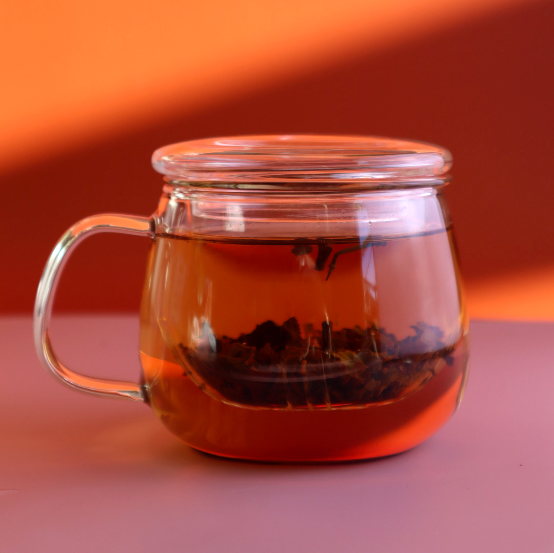 Glass tea cup infuser with lid on a pink table and orange background by Citea.